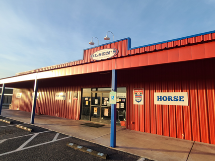 ClarkdaleThe exterior of Olsen's Clarkdale, featuring a bright red corrugated metal wall and roof, with a blue support pole in the foreground and a 'HORSE' sign on the right.